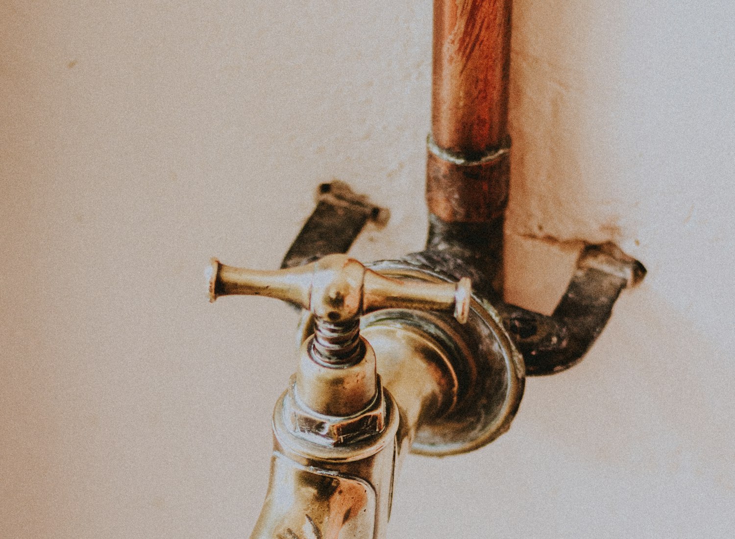 Copper supply pipe and aged brass isolation valve mounted on cream plaster, revealed during work on an older domestic property