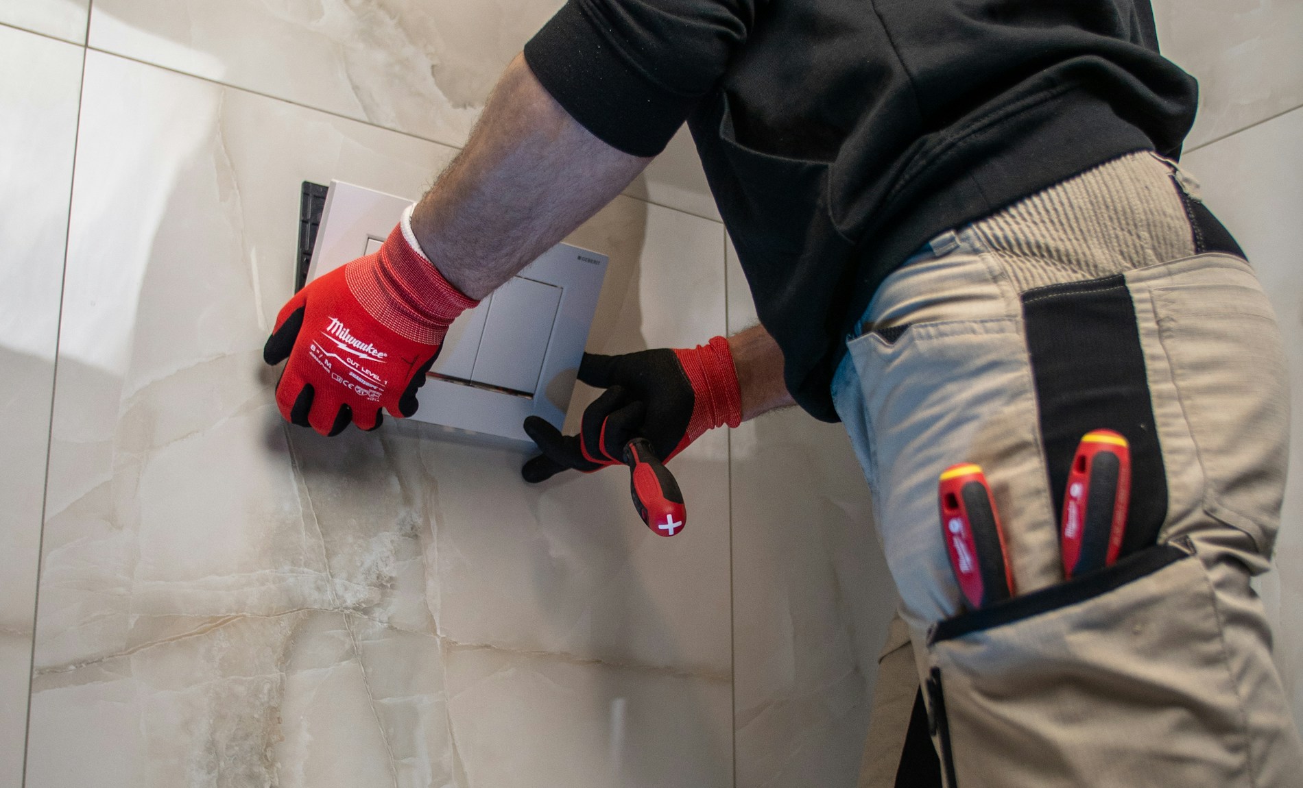 A tradesperson fitting a concealed cistern flush plate into tiled bathroom walls