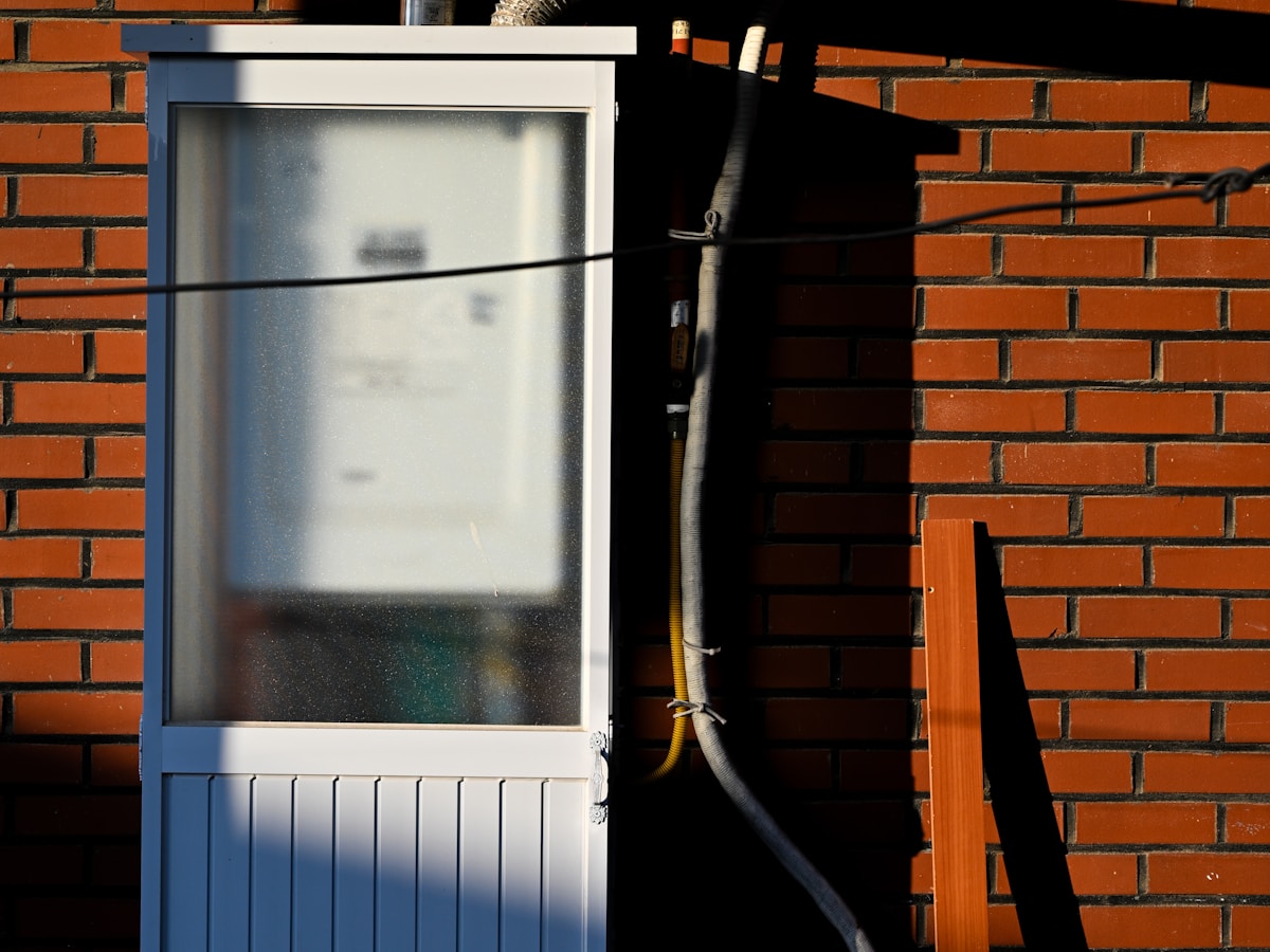 Gas meter cupboard with yellow supply pipe on the exterior of a brick terrace