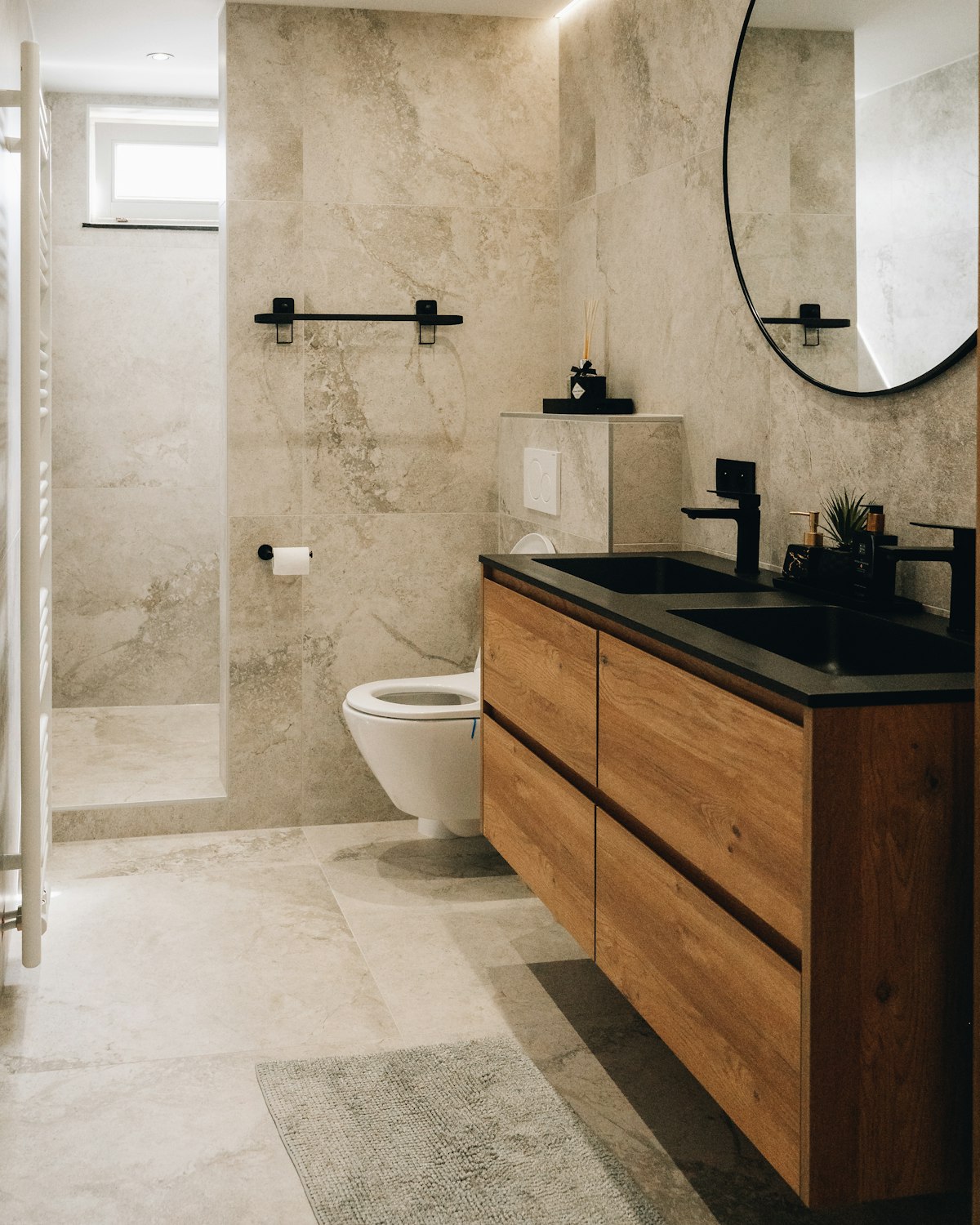 En suite refit with large travertine stone tiles, wall-hung toilet and dark timber double vanity with black stone worktop